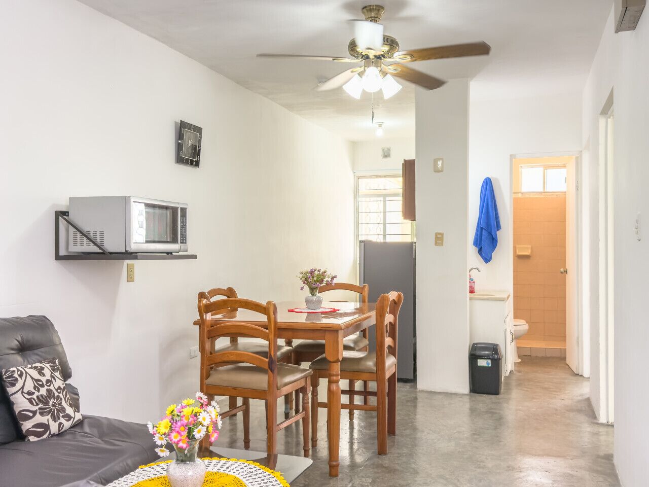 A compact living space with a dining area, a sofa, a ceiling fan, and a microwave.
