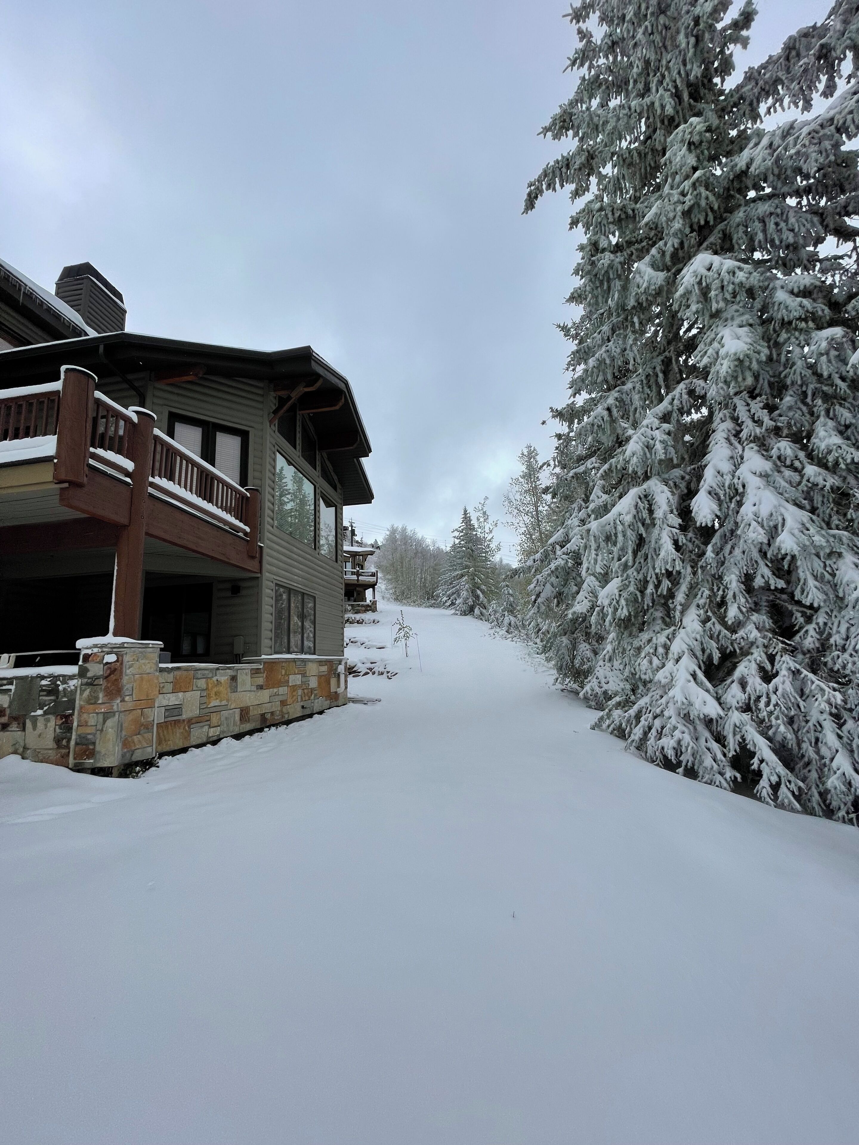 A snow-covered landscape with a house featuring a stone foundation and a wooden balcony.