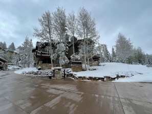 En stuga med en fasad av sten, en träveranda och snötäckta träd.