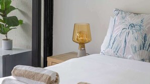 A hotel room with a bed, two rolled towels, a bedside lamp, a potted plant, and a window with curtains. - Easy Stay Pool, Esplanade Views (Cairns City)