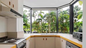 A kitchen with a view of palm trees, a stove, oven, and a microwave. - Easy Stay Pool, Esplanade Views (Cairns City)