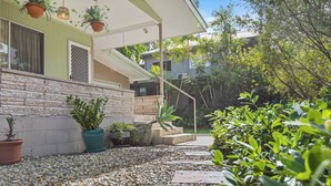 A house with a stone facade, a covered porch, and a gravel pathway leading to a staircase. - The Tides - 70s Seaside Bungalow (Port Douglas)