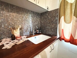 A kitchen with a tiled backsplash, a wooden countertop, a sink, and cabinets. - The Tides - 70s Seaside Bungalow (Port Douglas)