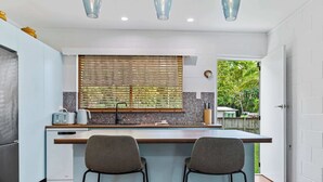 A modern kitchen with a central island, two bar stools, and pendant lighting. - The Tides - 70s Seaside Bungalow (Port Douglas)