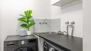 A compact kitchen with a washing machine, a sink, and a potted plant. - Easy Stay Pool, Esplanade Views (Cairns City)