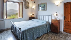 A bedroom with a bed, a nightstand, a dresser, a window with a view, and a stone wall. - Wonderful private villa for 8 people with WIFI, A/C, private pool, TV and pets allowed (Roccastrada)