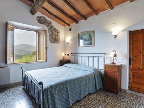 Camera da letto con un letto, un comodino, una cassettiera, una finestra vista e un muro in pietra.