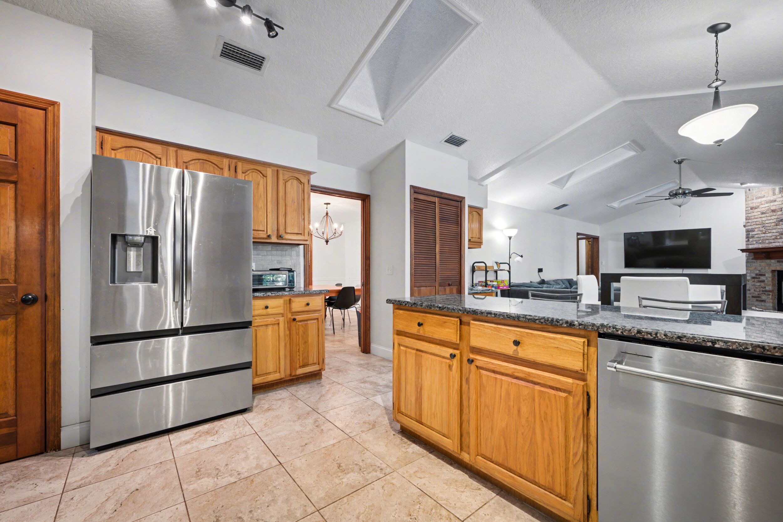 A modern kitchen with stainless steel appliances, wooden cabinets, and a dining area with a chandelier.
