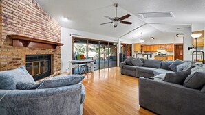 A spacious living area with a fireplace, a ceiling fan, and a kitchen in the background. - DeLand Spring House — Pool, 3/3.5, Near Blue Spring Manatees (DeLand)