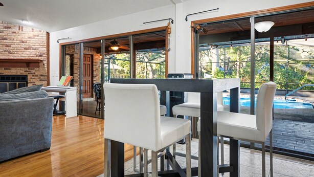 A modern living room with a fireplace, a pool view, and a dining area with white chairs. - DeLand Spring House — Pool, 3/3.5, Near Blue Spring Manatees (DeLand)