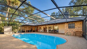 An indoor swimming pool with a glass ceiling, surrounded by a patio area with seating and a brick wall. - DeLand Spring House — Pool, 3/3.5, Near Blue Spring Manatees (DeLand)