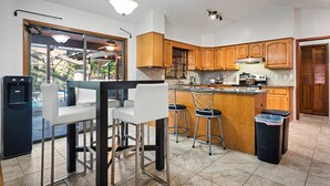 A kitchen with wooden cabinets, a bar area with stools, a refrigerator, and a trash bin. - DeLand Spring House — Pool, 3/3.5, Near Blue Spring Manatees (DeLand)