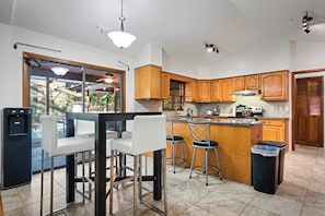 A kitchen with wooden cabinets, a bar area with stools, a refrigerator, and a trash bin. - DeLand Spring House — Pool, 3/3.5, Near Blue Spring Manatees (DeLand)