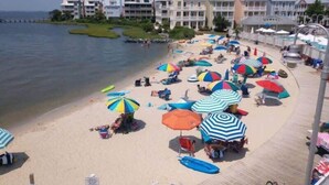 Une plage avec des parasols et des chaises longues, une jetée et une rangée de bâtiments en arrière-plan.