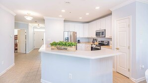 Une cuisine moderne avec des meubles blancs, un îlot central et un panneau indiquant « Bienvenue ».