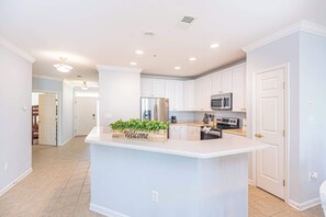 A modern kitchen with white cabinetry, a central island, and a 'Welcome' sign. - 3BR Resort Condo with Pools by Beach (Ocean City)