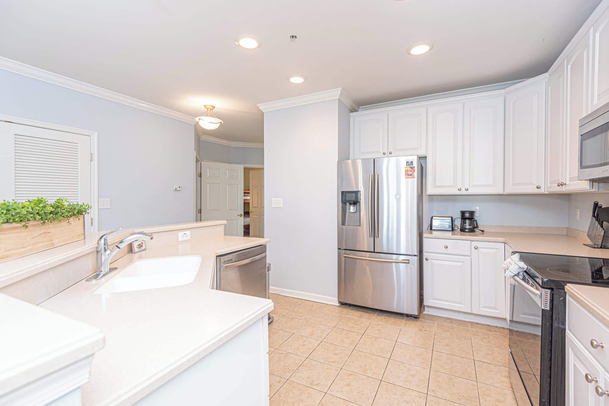 A modern kitchen with white cabinets, stainless steel appliances, and a tiled floor.