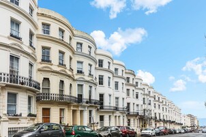 Una hilera de edificios blancos con balcones, coches aparcados y cielo despejado.