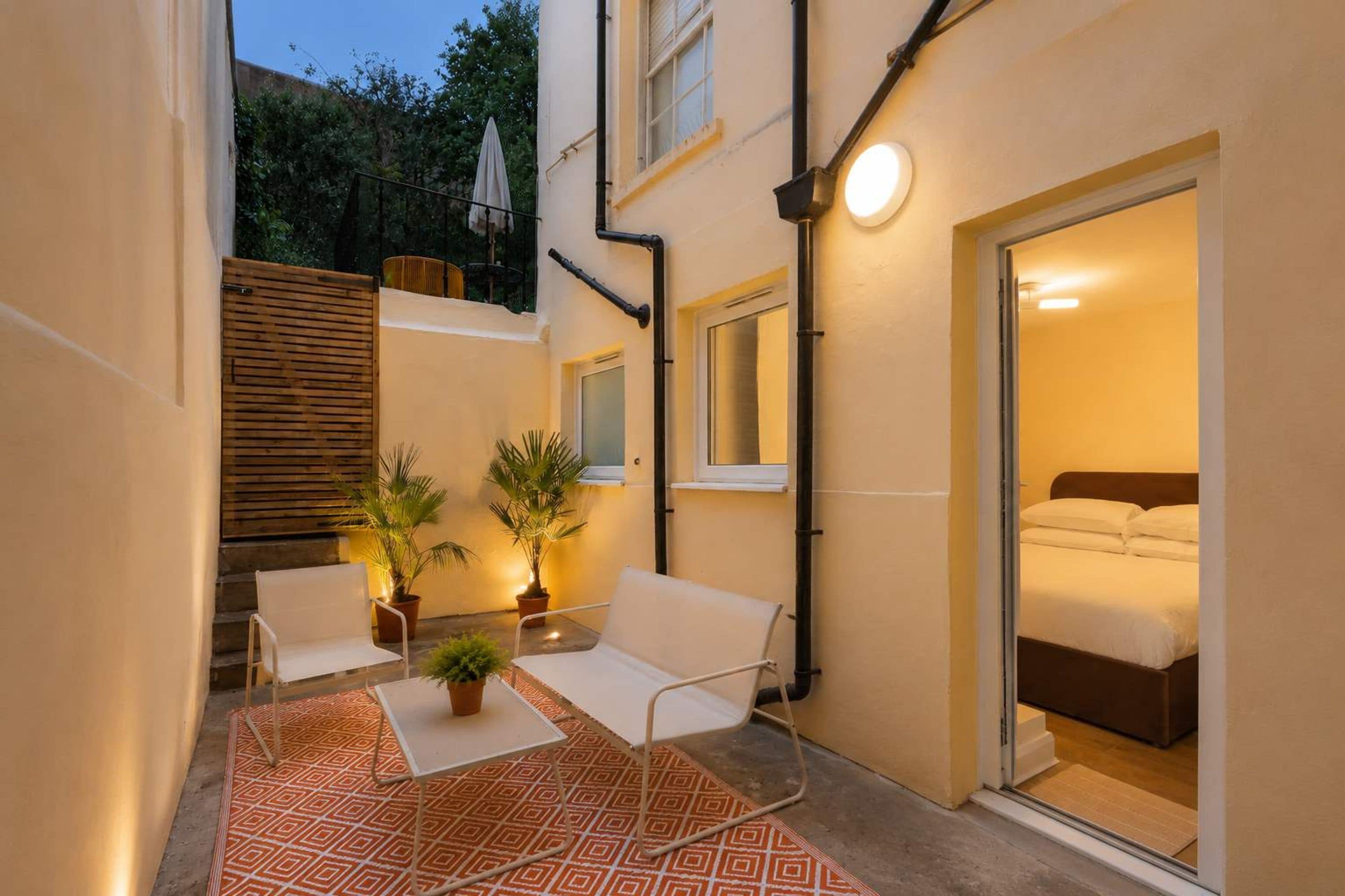 A small, well-lit courtyard with a sofa, two potted plants, and a table.