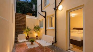 A small, well-lit courtyard with a sofa, two potted plants, and a table.