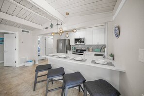 Eine moderne Küche mit einer zentralen Kochinsel, Barhocker, Edelstahlgeräten und einer weißen Decke.