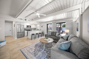 Ein geräumiger Wohnbereich mit grauem Sofa, einem Couchtisch und einer Küche mit weißen Schränken und Edelstahlgeräten.