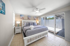 A bedroom with a bed, nightstands, a ceiling fan, and a sliding glass door to an outdoor area. - The Salt & Sand Beach Shack: Modernized 1950s Duplex – 1.4 Mi to Siesta Beach (Siesta Key)