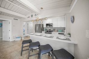 A modern kitchen with a central island, bar stools, and a stainless steel refrigerator. - Salt & Sand Beach Shack: Modernized Siesta Duplex (Siesta Key)