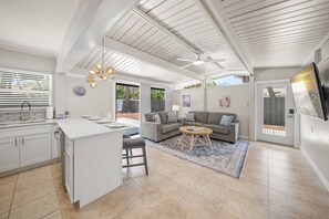 Eine geräumige Küche mit einer zentralen Kochinsel, einem Essbereich mit grauem Sofa und einem Deckenventilator.