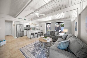 Eine moderne Küche mit Edelstahlgeräten, ein Essbereich mit grauem Sofa und Couchtisch sowie ein Deckenventilator.