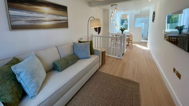 Ein modernes Wohnzimmer mit einem weißen Sofa, einem großen abstrakten Gemälde, einer Stehlampe und einem Essbereich im Hintergrund.