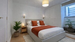 Ein Schlafzimmer mit Bett, Nachttischen, einem Fenster und einem Blumentopf.