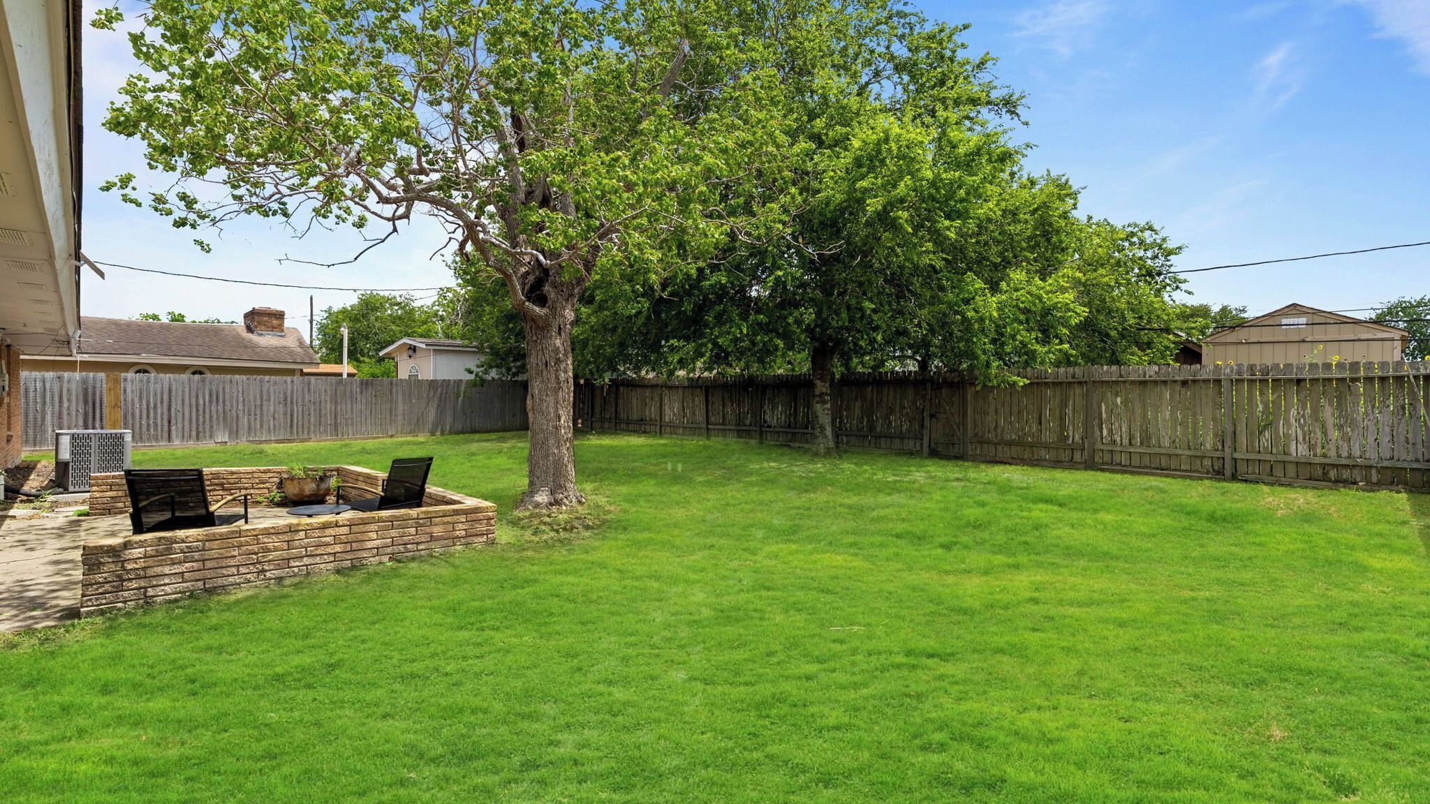 Un patio trasero con un árbol, una jardinera de ladrillo y una valla de madera.