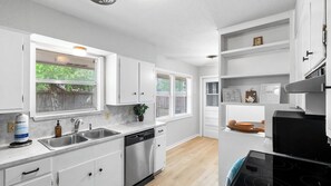 A modern kitchen with white cabinets, a dishwasher, a stove, and a window with blinds.