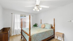 A four-poster bed with a patterned bedspread, a ceiling fan, and a small wooden side table.