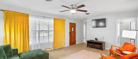 A living room with a ceiling fan, a TV, a sofa, a coffee table, and a dining area with chairs.