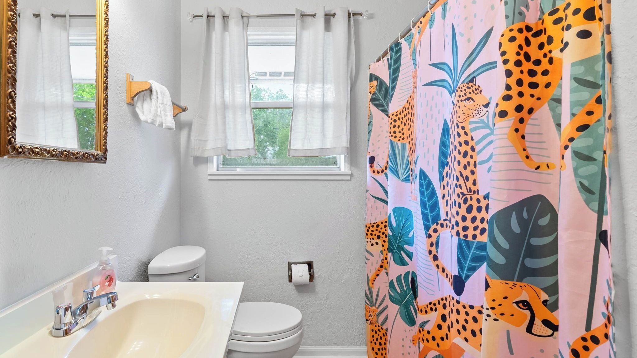 Een badkamer met een witte wastafel, toilet en douchegordijn met luipaardprint.