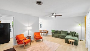 A modern living room with a sofa, two armchairs, a dining table, and a ceiling fan.