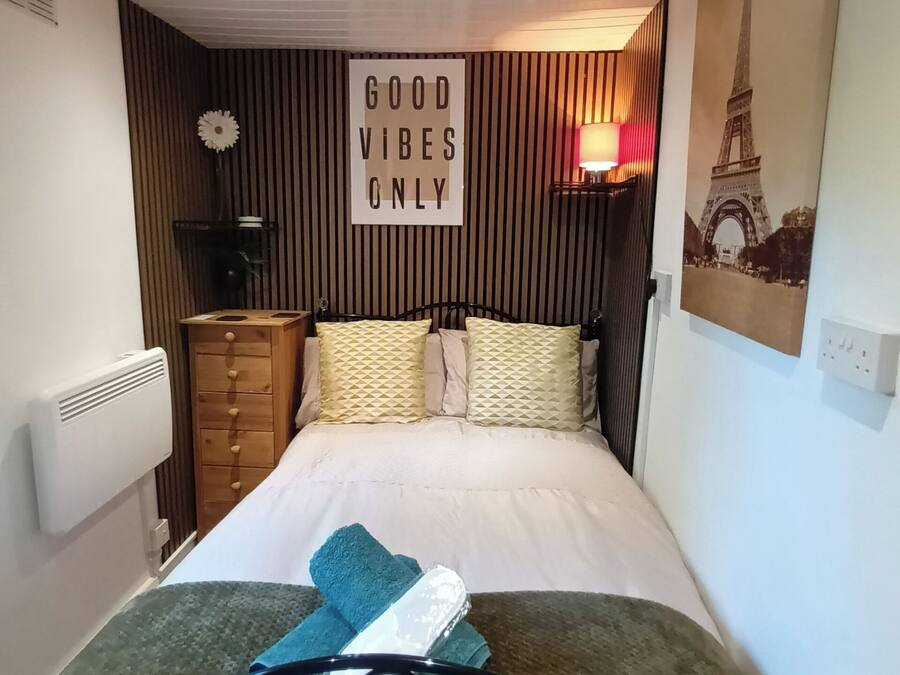 A bedroom with a bed, a dresser, a radiator, a wall with a 'GOOD VIBES ONLY' sign, and a lamp.
