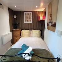 A bedroom with a bed, a dresser, a radiator, a wall with a 'GOOD VIBES ONLY' sign, and a lamp.
