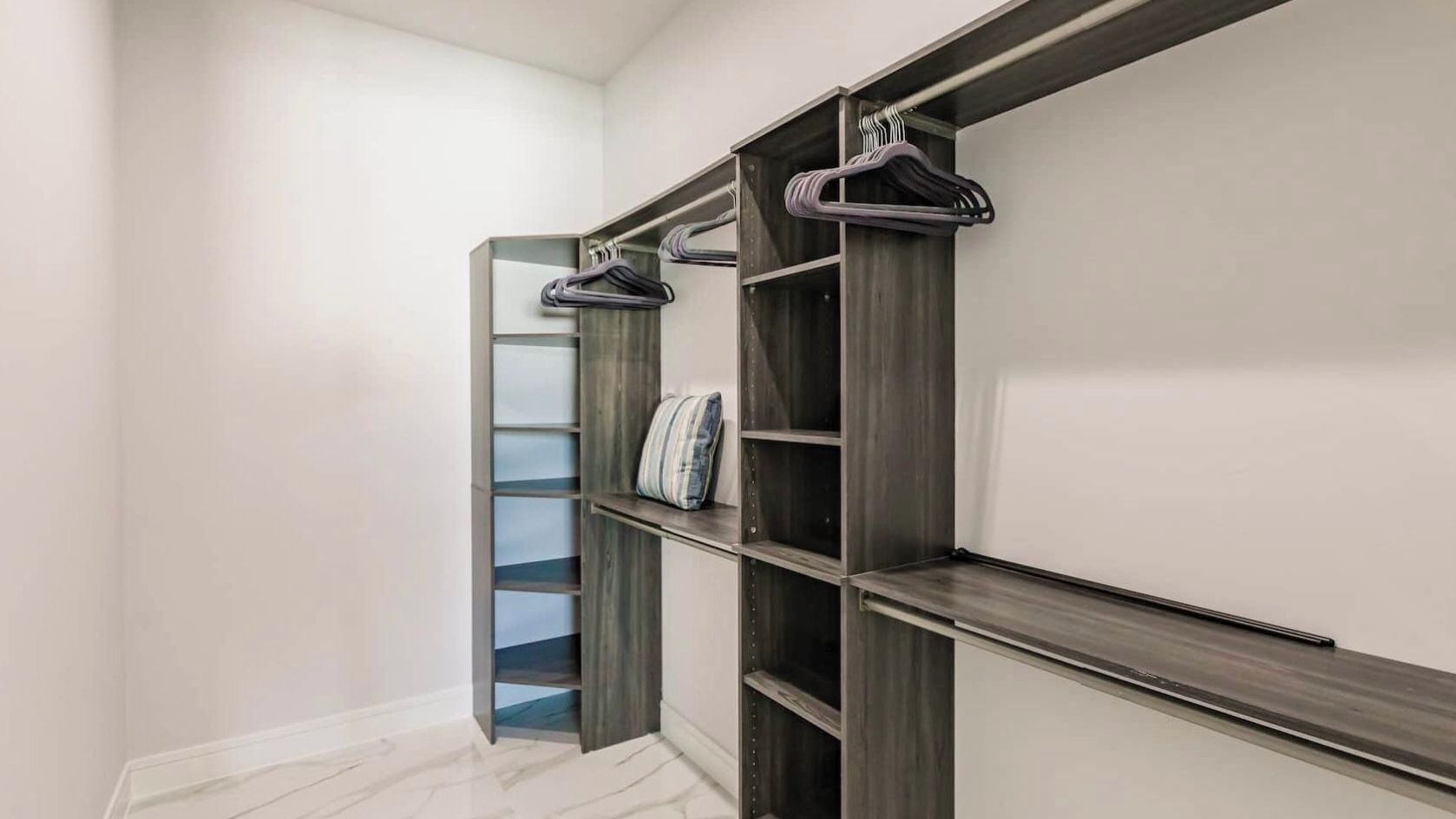 A walk-in closet with open shelving, a hanging rod, and a door leading to another room.
