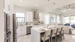 Une cuisine moderne avec des meubles blancs, un îlot central et un coin repas comprenant des chaises et une table pour quatre personnes.