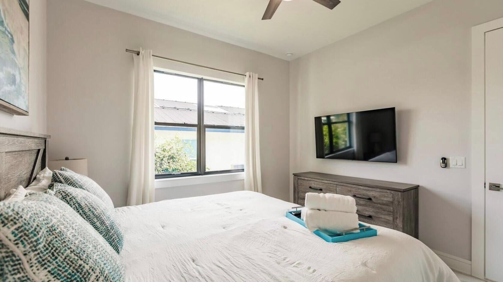 A bedroom with a bed, a TV, a window, and a ceiling fan.
