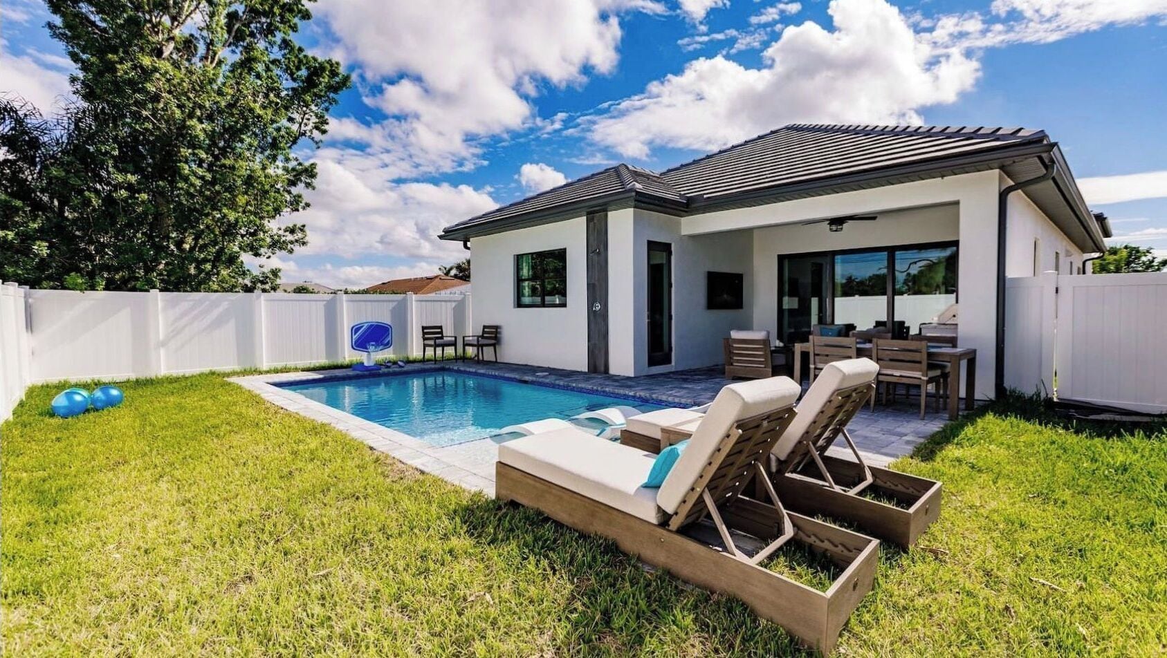 A modern house with a swimming pool, outdoor seating, and a fenced backyard.