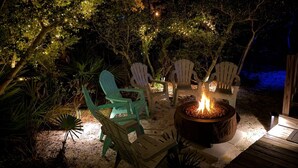 An outdoor seating area with chairs and a fire pit surrounded by trees and string lights. - Welcome to Drift & Tide Cottage, your quiet coastal escape in Fort Morgan. (Gulf Shores)