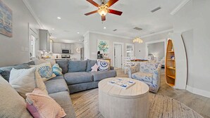 A spacious living room with a grey sectional sofa, a round coffee table, and a ceiling fan. - Welcome to Drift & Tide Cottage, your quiet coastal escape in Fort Morgan. (Gulf Shores)