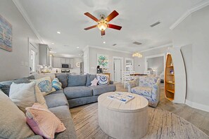 A spacious living room with a grey sectional sofa, a round coffee table, and a ceiling fan. - Welcome to Drift & Tide Cottage, your quiet coastal escape in Fort Morgan. (Gulf Shores)