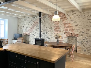 Eine moderne Küche mit einer großen Kochinsel, einer Steinwand, einem Kamin aus Backsteinen und einer hängenden Pendelleuchte.