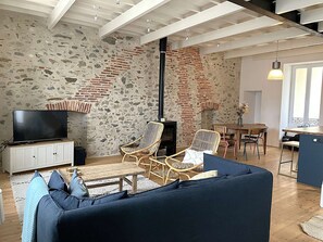 Ein Wohnzimmer mit Steinwand, Fernseher, Korbstühlen, einer Couch und einem Essbereich mit Tisch und Stühlen.