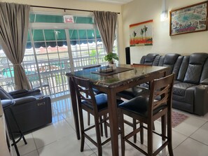 A room with a glass-top table, wooden chairs, a sofa, and a view through a window with a 'No Smoking' sign. - Hip Strip Vibe (Montego Bay)